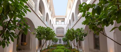 A courtyard with white walls, arches, and a central garden with plants and flowers.