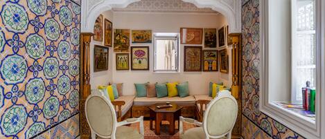 Una habitación con pared de baldosas estampadas, un sofá con cojines, una mesa de madera y sillas.
