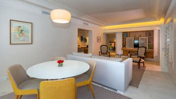 A modern living room with a round white table, yellow chairs, a grey sofa, and a dining area with a white table and chairs.