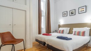 Een hotelkamer met twee bedden, een bruine leren fauteuil en een raam met gordijnen.