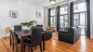 Een moderne woonkamer met een eettafel, stoelen, een bank en een groot raam met gordijnen.