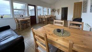A spacious dining area with wooden tables and chairs, large windows, and a view of the outdoors. - Dalshöfði Guesthouse (Kirkjubæjarklaustur)