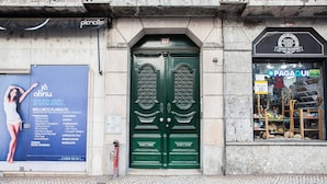 Une porte verte à deux battants, avec une plaque au-dessus, et un magasin sur la droite, dont l’enseigne indique « PAGAQUI ».