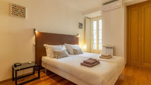 Un lit double avec du linge de lit blanc, une table de chevet avec une lampe et un plancher en bois.