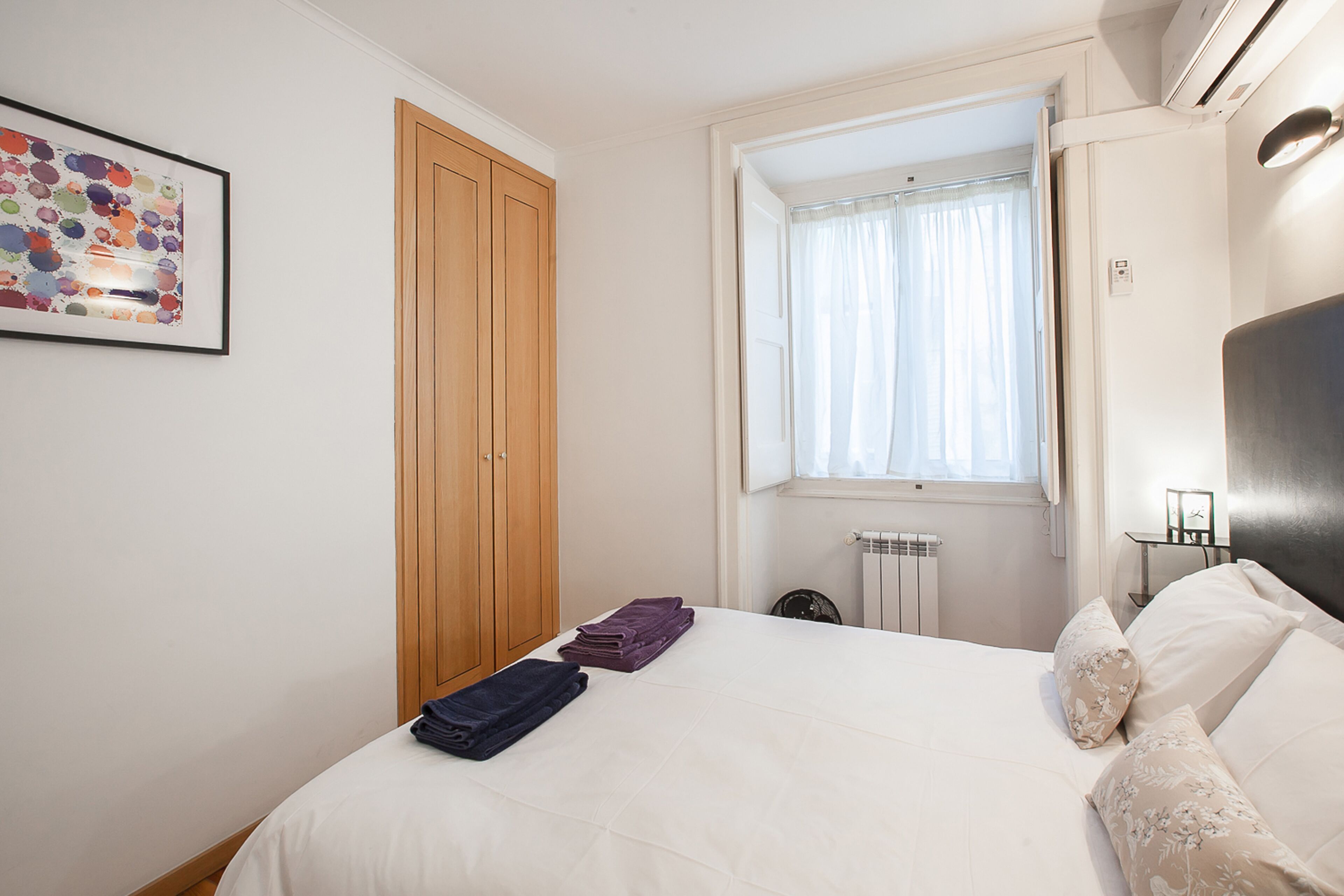 A bedroom with a bed, a wooden wardrobe, a window with curtains, and a radiator.