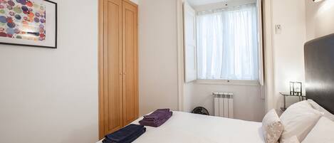 A bedroom with a bed, a wooden wardrobe, a window with curtains, and a radiator.