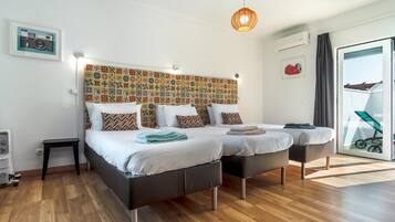 A room with two beds, a patterned headboard, a small table, and a view of the outside.