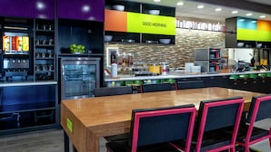 A modern kitchen with a wooden table and black chairs, a refrigerator, and a sign that says "GOOD MORNING". - Home2 Suites by Hilton Oklahoma City NW Expressway (Oklahoma City)