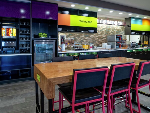 Una cocina moderna con una mesa de madera y sillas negras, un refrigerador y un letrero que dice “GOOD MORNING”.