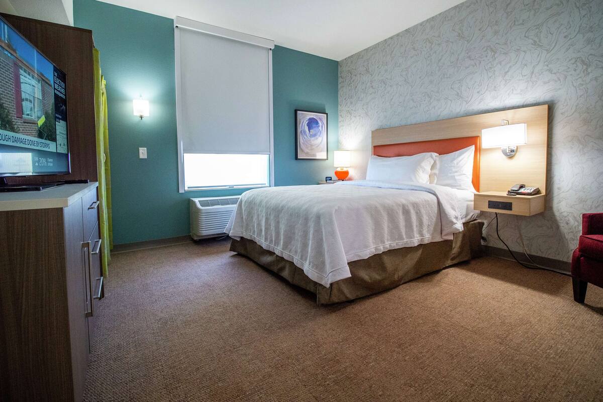 A hotel room with a bed, bedside table, lamp, and a TV on a stand.