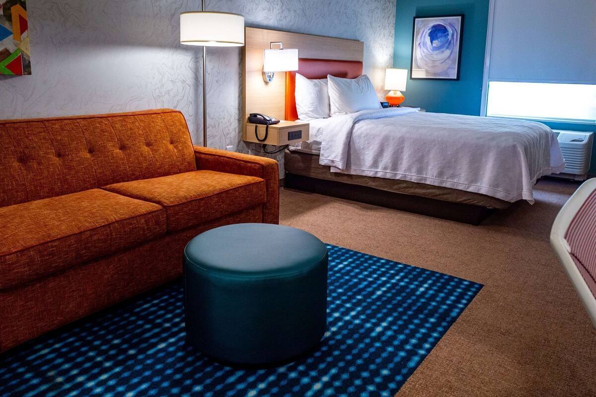 A hotel room with a sofa, a bed, a nightstand, a lamp, and a patterned rug.