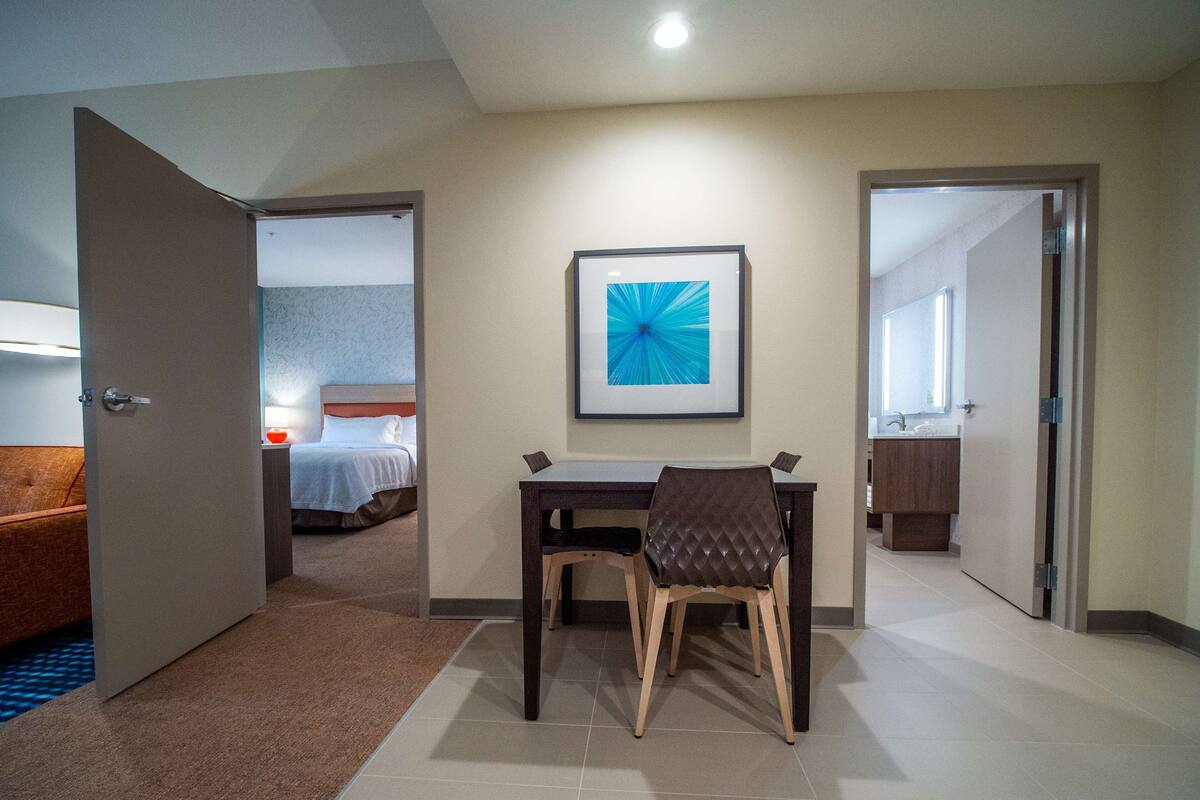 A hotel room with a bed, a desk with a chair, a framed picture on the wall, and a bathroom visible through an open door.