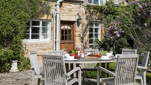 Un bâtiment en pierre avec une table et des chaises en bois disposées à l’extérieur.