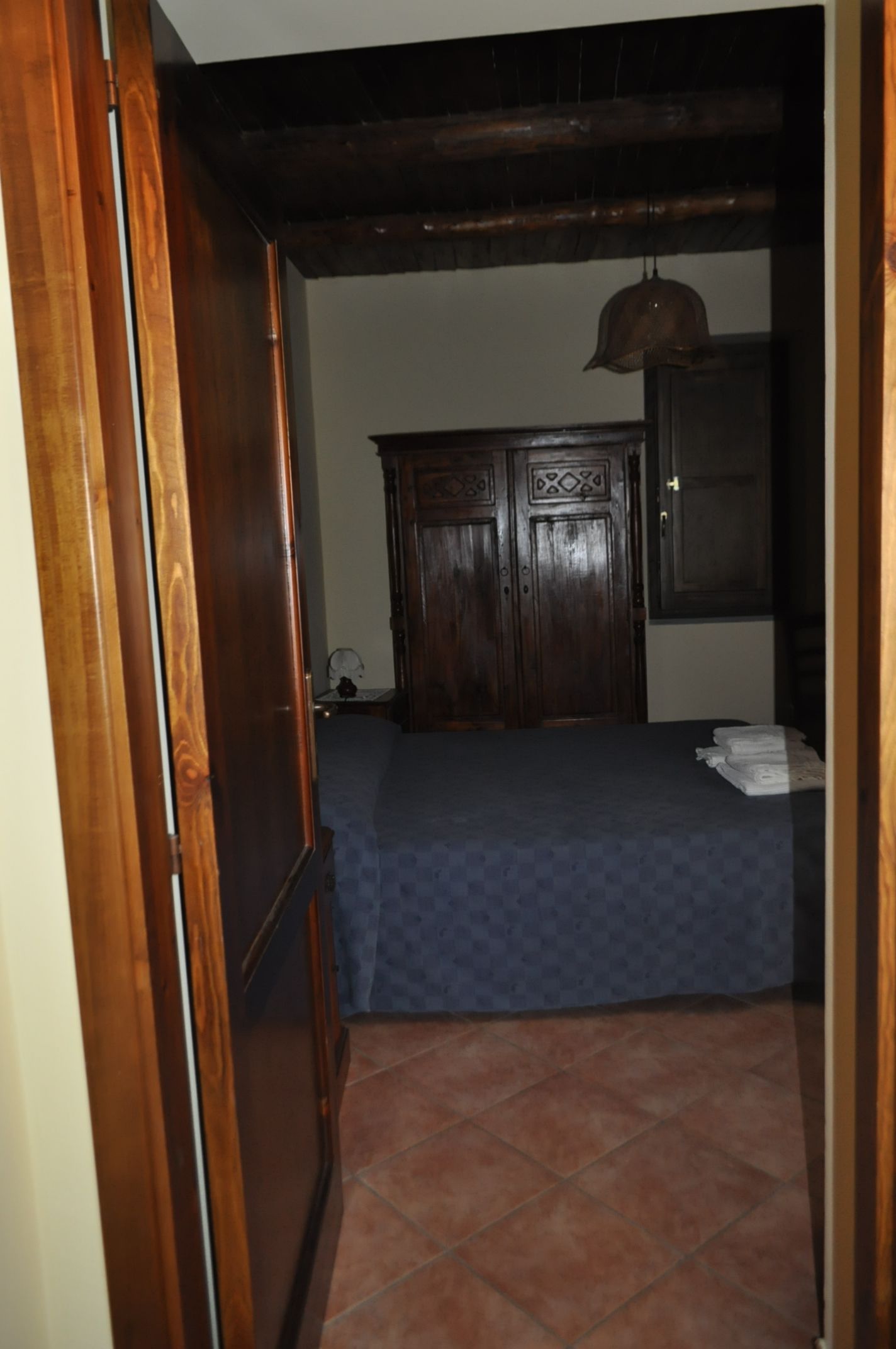 A room with a bed, a wooden wardrobe, and a tiled floor.