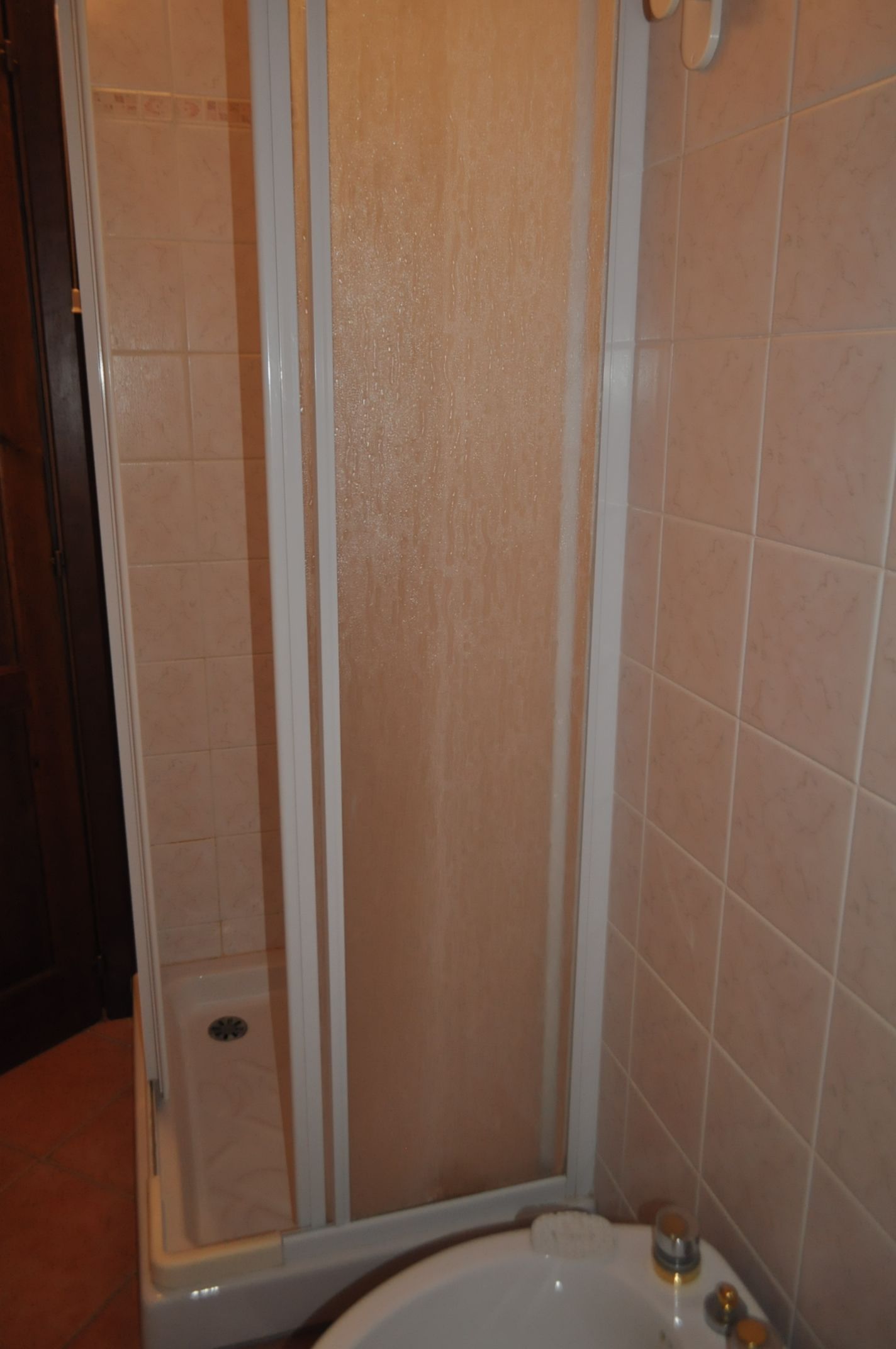 Box doccia con porta in vetro, vasca da bagno e pareti rivestite di piastrelle color beige.