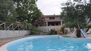 A swimming pool with a stone wall, trees, and a building in the background. - I Cedri (Orsomarso)