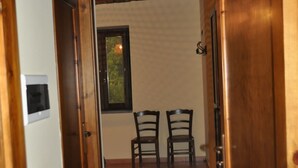 A hallway with wooden doors and a tiled floor leading to a room with two chairs and a window. - I Cedri (Orsomarso)