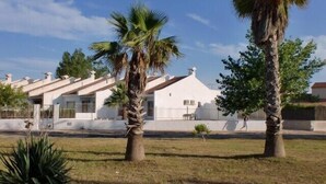 Una hilera de casas blancas con techos inclinados, rodeadas de palmeras y un césped.