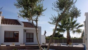 Una casa moderna con techo de tejas, paredes blancas y un pequeño jardín con piedras blancas y una palmera.