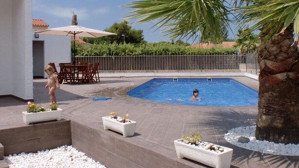 Una piscina con un niño y un adulto en el agua, rodeada de plantas y una palmera.
