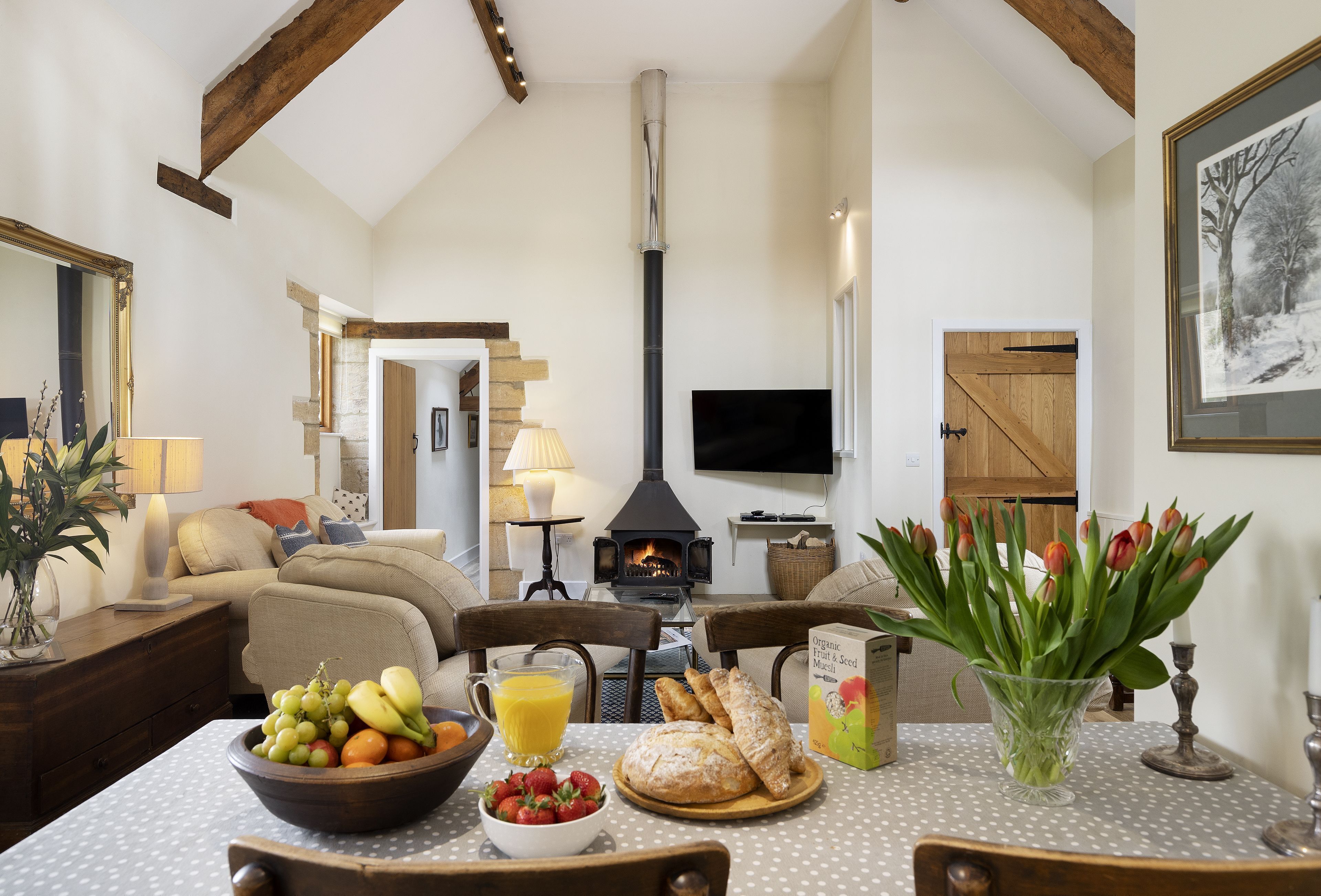 A cozy living room with a fireplace, a television, and a dining area with fruit and bread.