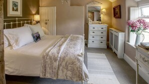 A bedroom with a bed, dresser, radiator, and a window with flowers.