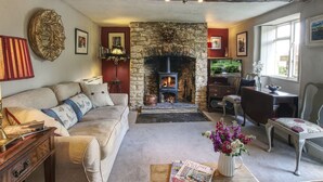 A cozy living room with a stone fireplace, a sofa, a coffee table with magazines, and a dining area with a table and chairs.