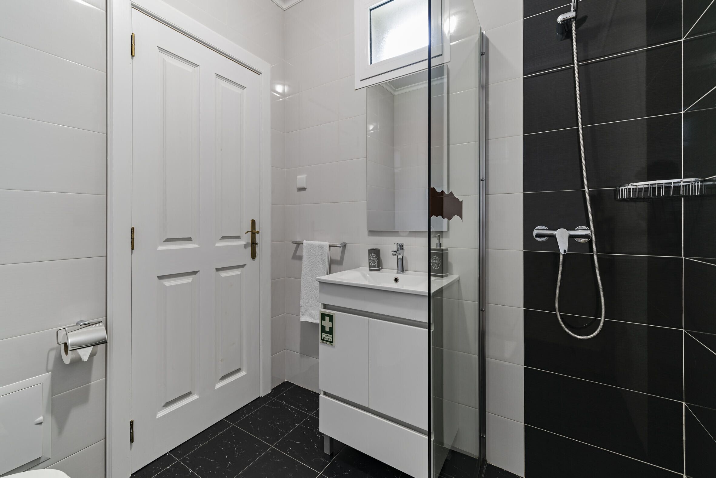 Een moderne badkamer met een witte wastafel, een douchecabine van glas en zwart betegelde wanden.