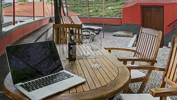 Een houten tafel met een laptop, wijnglazen en een fles Madeira.