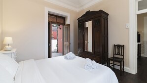 Een hotelkamer met een net opgemaakt bed, een houten garderobe en een stoel.
