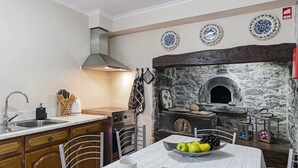 Een keuken met een oven in een stenen muur, houten kastjes en een eethoek met een tafel voor twee personen.