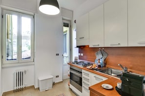 A modern kitchen with white cabinets, a gas stove, a sink, and a coffee machine.