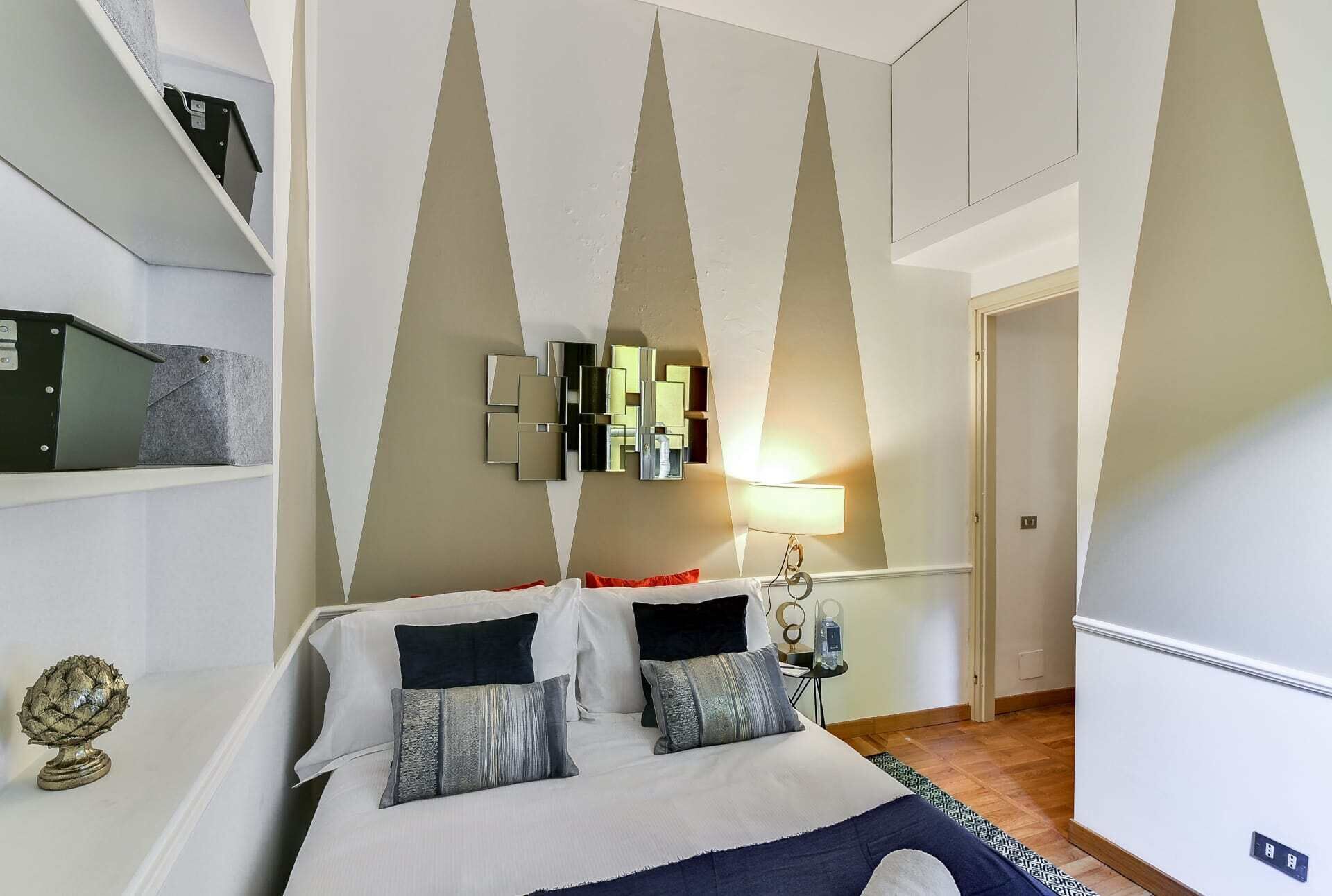 A modern bedroom with a bed, a wall-mounted light, and a decorative wall piece.