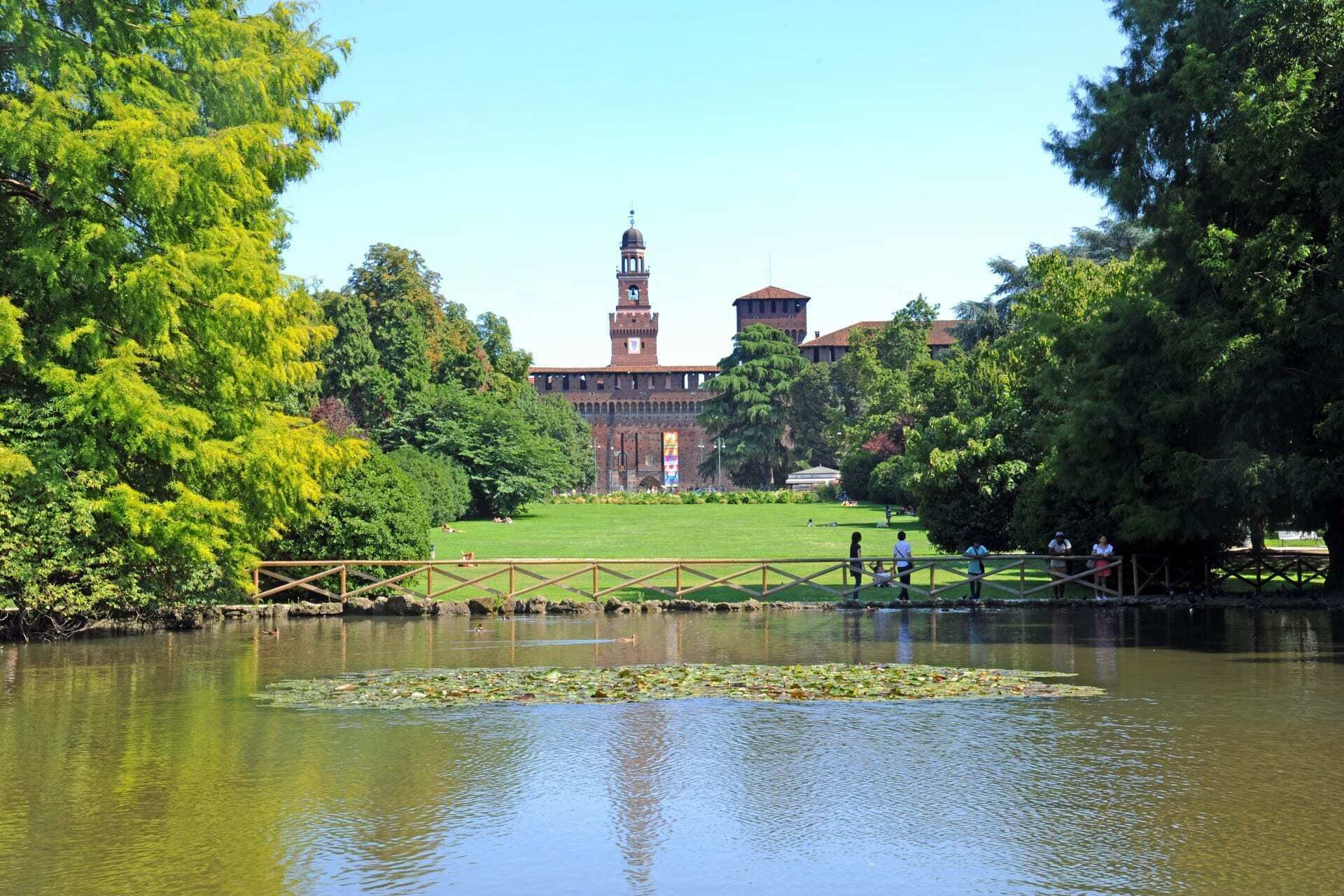 A historic building with a prominent tower, surrounded by lush greenery and a calm water body.