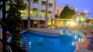 A swimming pool with lounge chairs and a poolside area, surrounded by buildings with balconies and outdoor seating. - Meryemana Hotel (Didim)