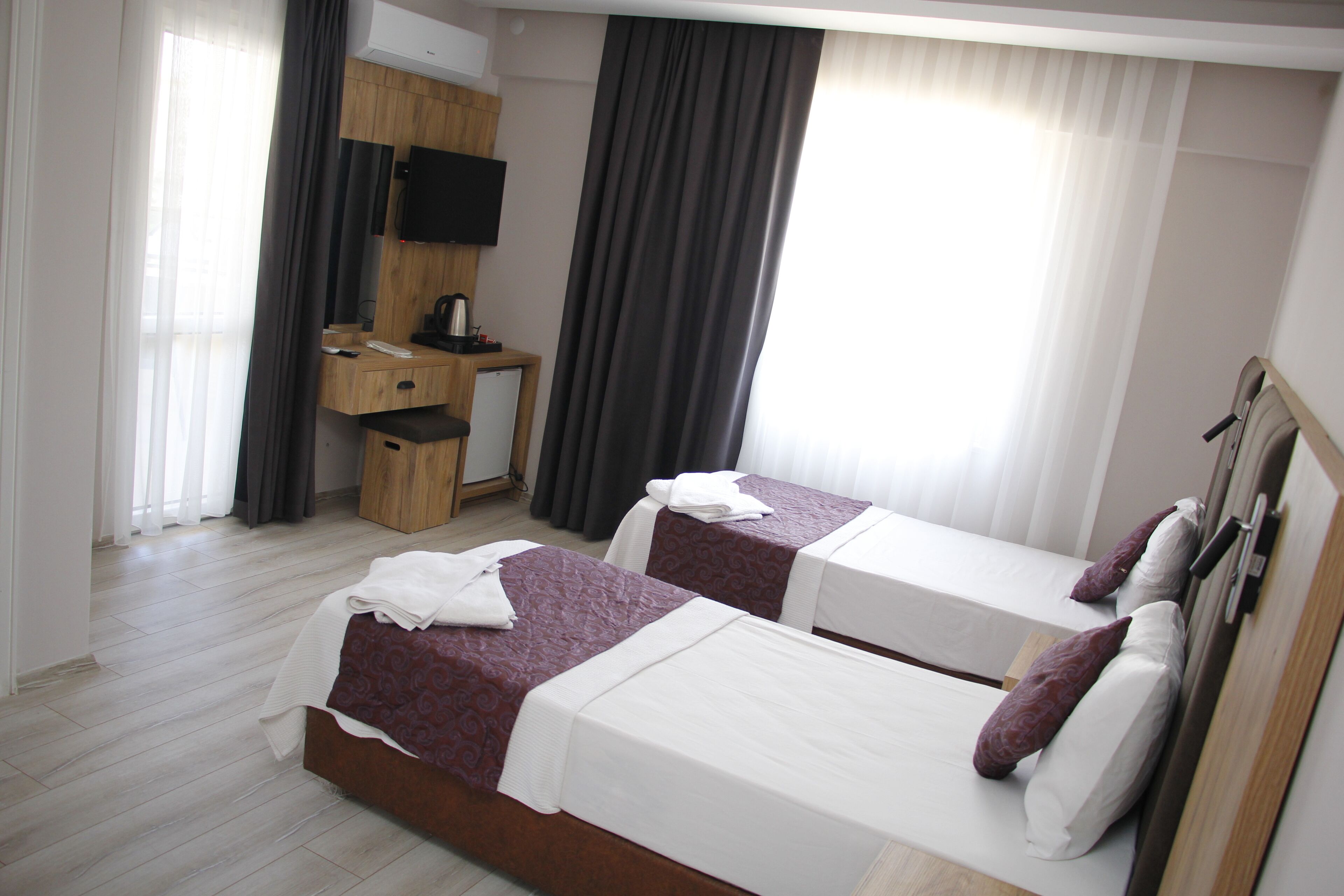 Una habitación de hotel con dos camas, un escritorio, un televisor y un ventanal con cortinas.