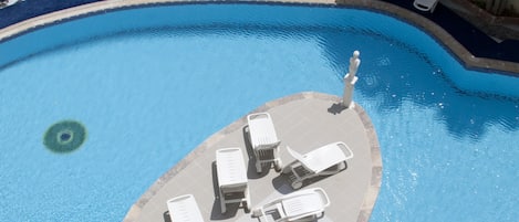 Una piscina con sillas de descanso dispuestas en semicírculo, suelo a cuadros y agua cristalina.