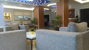 A lobby with grey upholstered sofas, a small table with a yellow pot, and potted plants. - Meryemana Hotel (Didim)