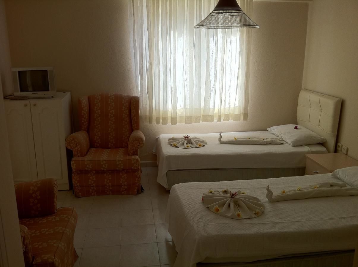 Una habitación de hotel con dos camas, una silla, un televisor y una ventana con cortinas translúcidas.