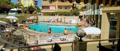 A pool area with lounge chairs and umbrellas, a diving board, and a view of the surrounding buildings.
