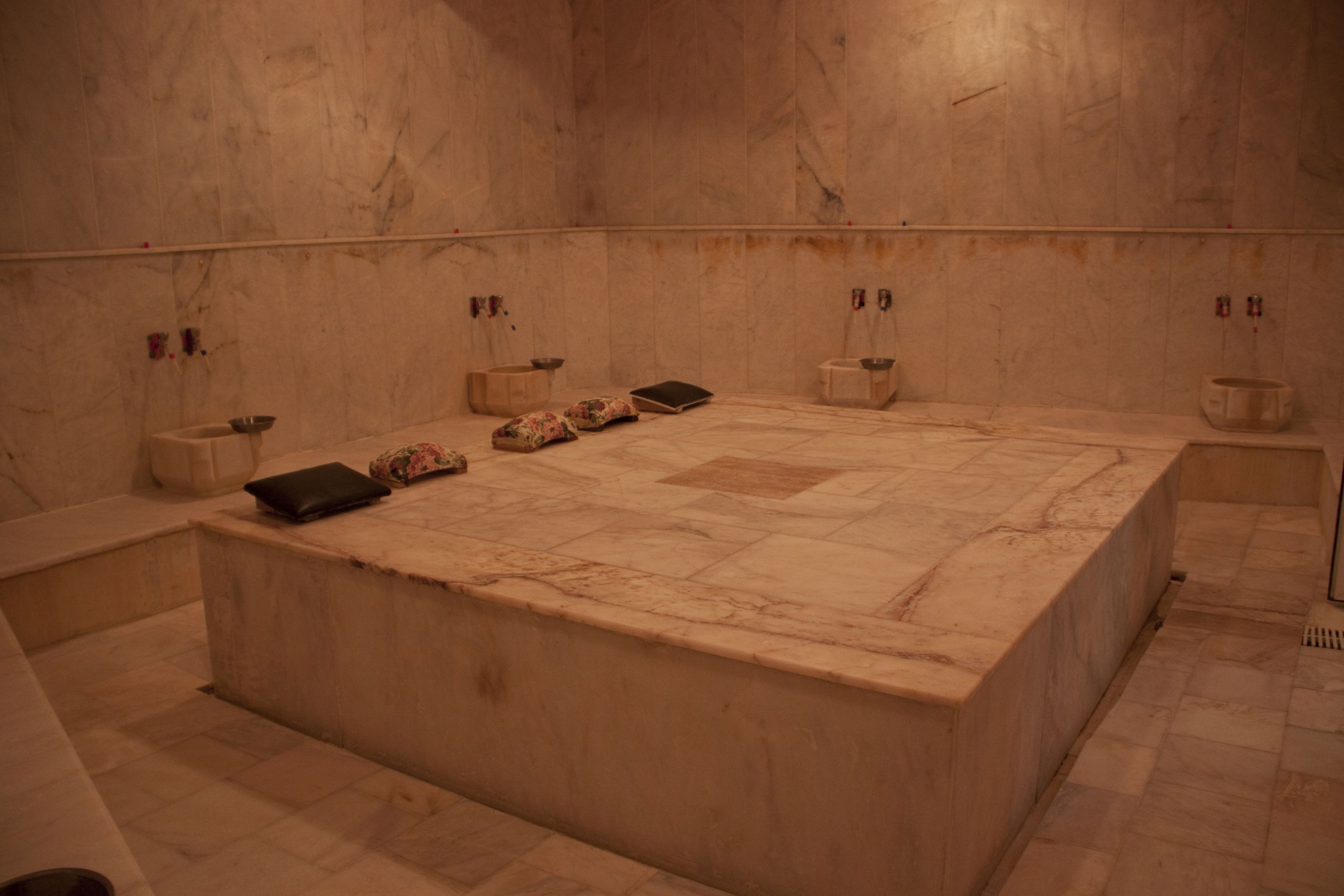 A large marble-tiled room with a central seating area, two small side tables, and a bench.