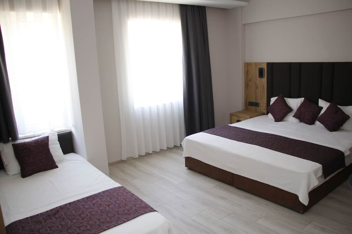 A hotel room with two beds, a wooden headboard, a nightstand, and a window with curtains.