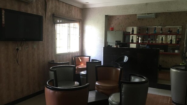 Ein Wohnzimmer mit Fernseher, Fenster und Küchenzeile mit Arbeitsfläche und Regalen.