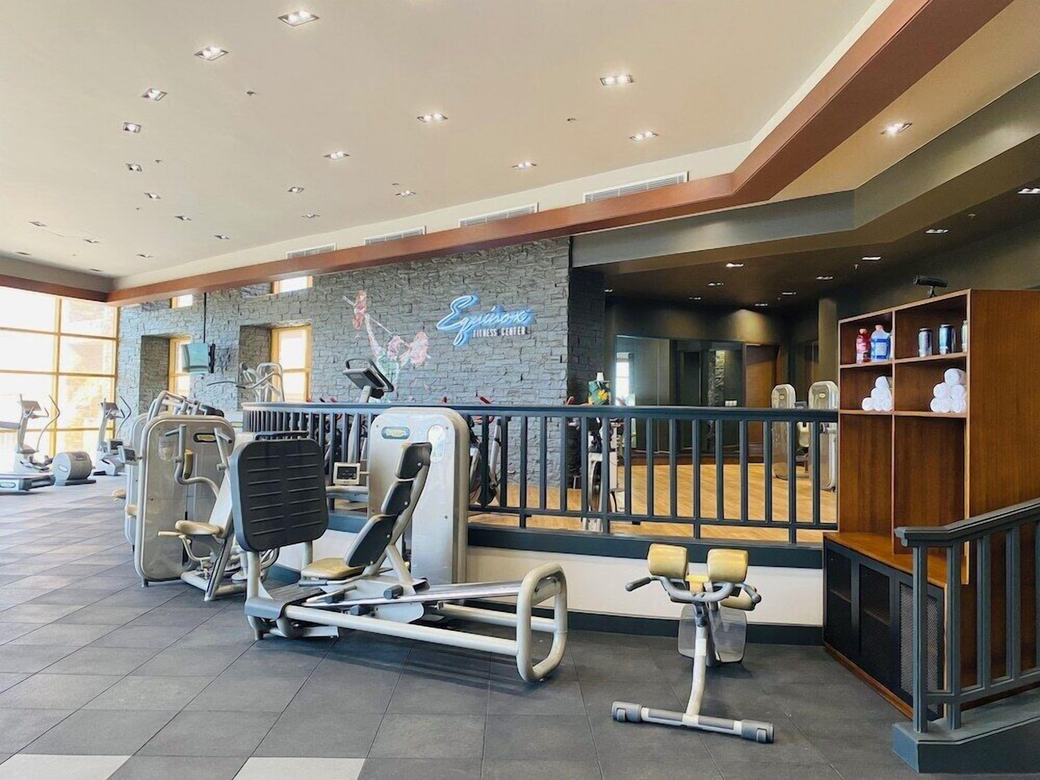 A fitness center with cardio machines, a wall with a logo, and a reception area with a counter and shelves.
