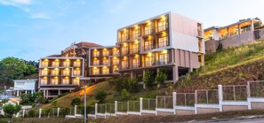 Ein mehrstöckiges Hotel mit Balkonen, einer flachen Dachterrasse und einer Hanglage.
