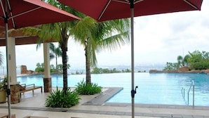 A poolside area with lounge chairs and umbrellas, a palm tree, and a view of a city skyline. - Timberland Heights (San Mateo)