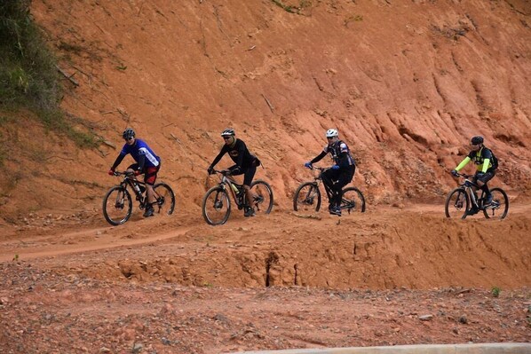 Four cyclists on a dirt road with a steep, red-brown hillside in the background. - Timberland Heights (San Mateo)