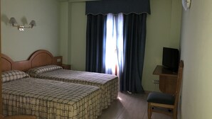 A hotel room with two beds, a TV, a chair, and a window with curtains. - Hotel Silos 2000 (Santo Domingo de Silos)