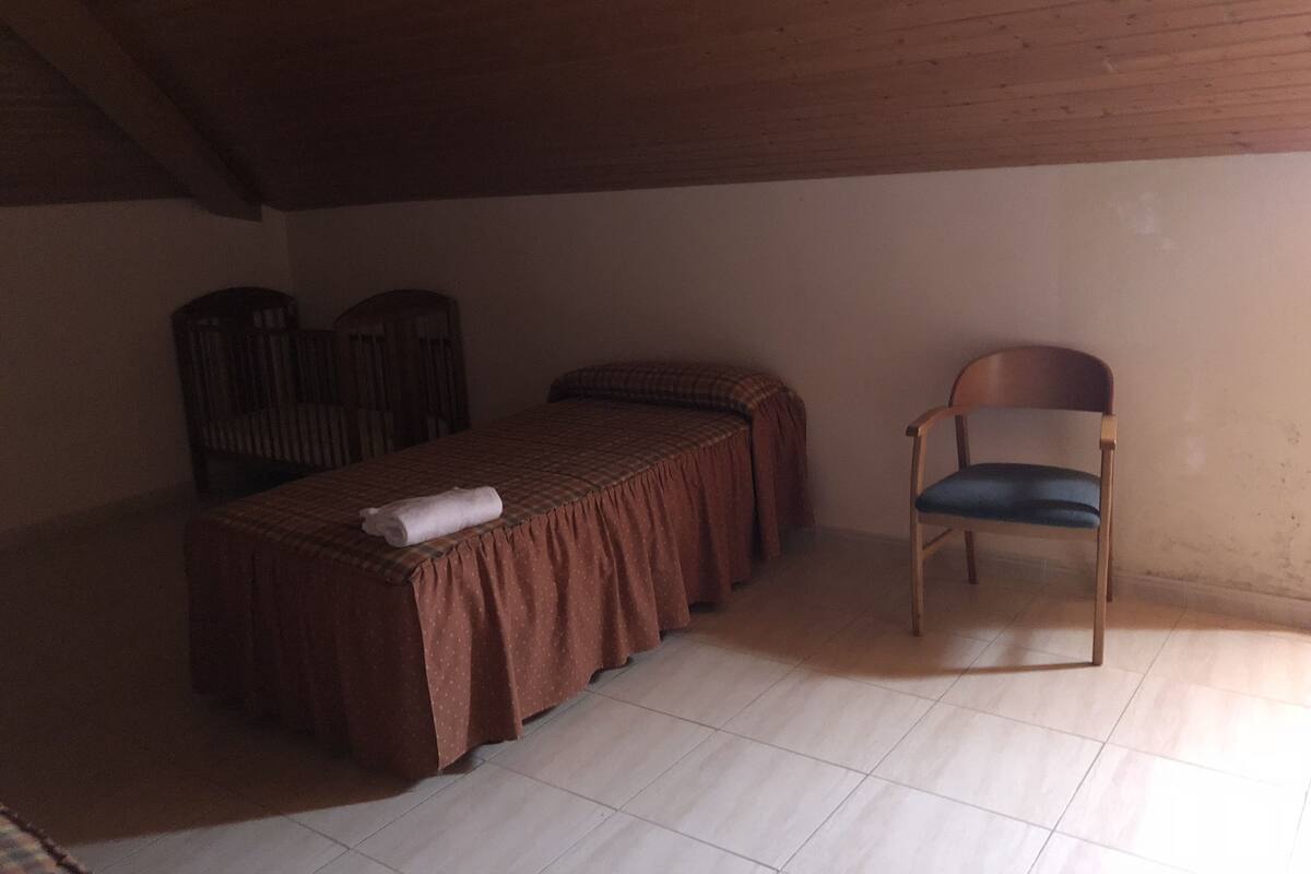 A small, dimly lit room with a single bed, a chair, and a small table.