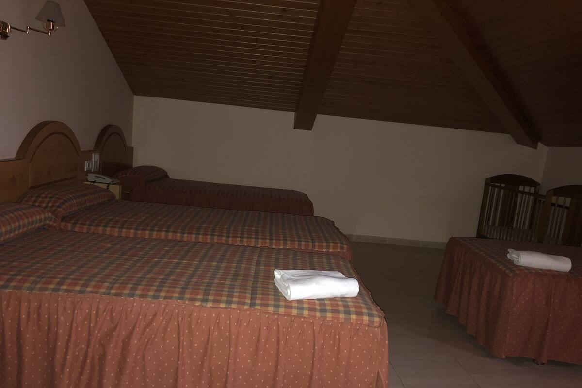 A room with two beds, each with a plaid bedspread, a small table with a towel, and a wooden ceiling.